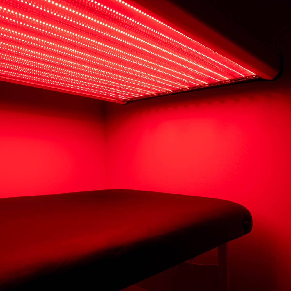A red and near-infrared LED light panel above a treatment couch